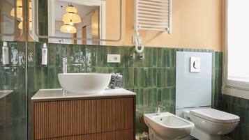 A modern bathroom with a large sink, bidet, and bathtub, featuring green tiled walls and a marble floor.