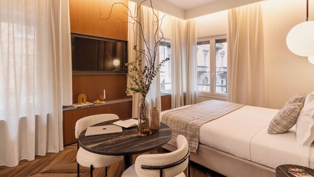 A modern hotel room with a bed, a desk with a chair, a TV, and a vase with branches. - LUMERA STAY - Brera (Milan)