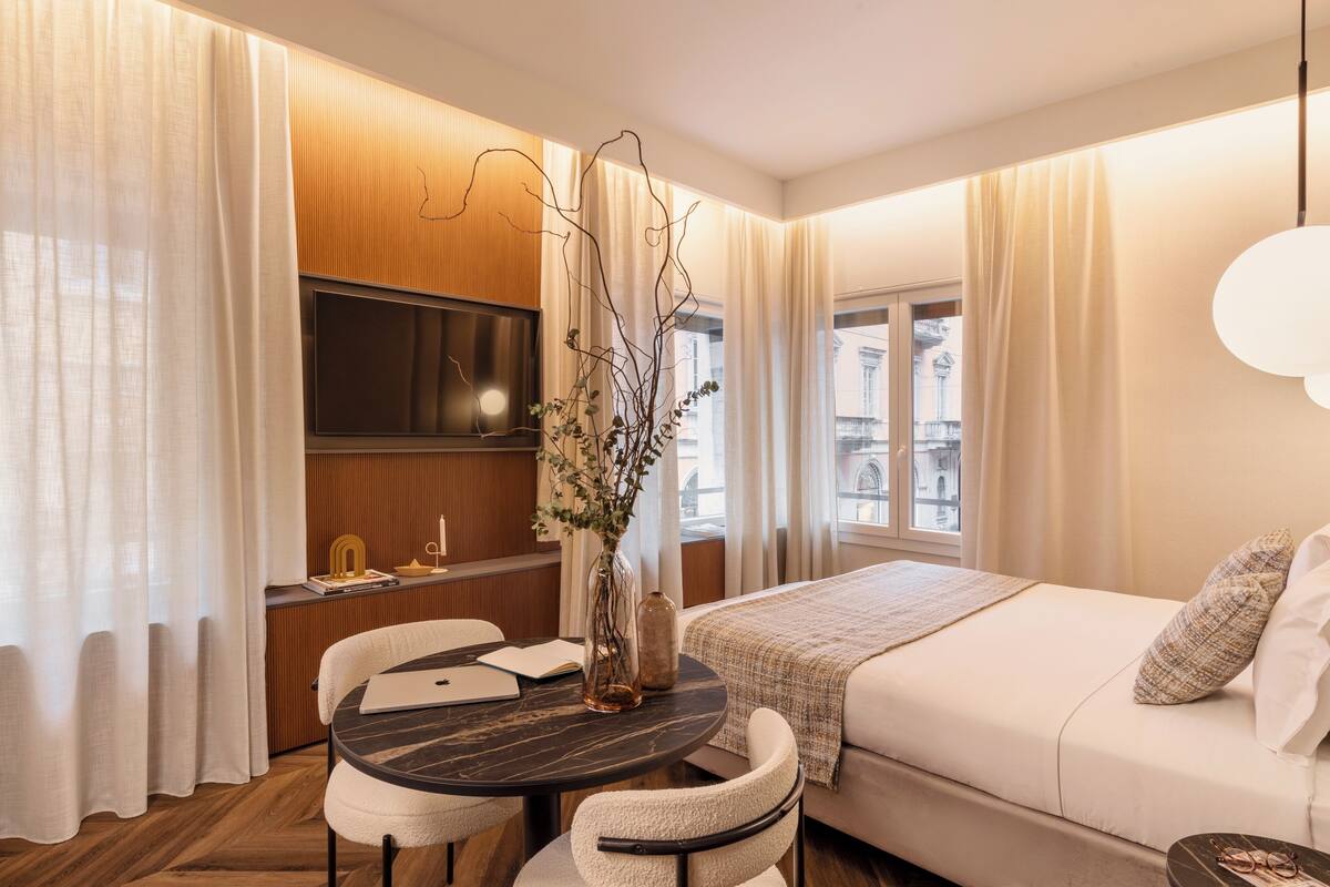 Habitación de hotel moderna con cama, escritorio con silla, televisor y un florero con ramas.