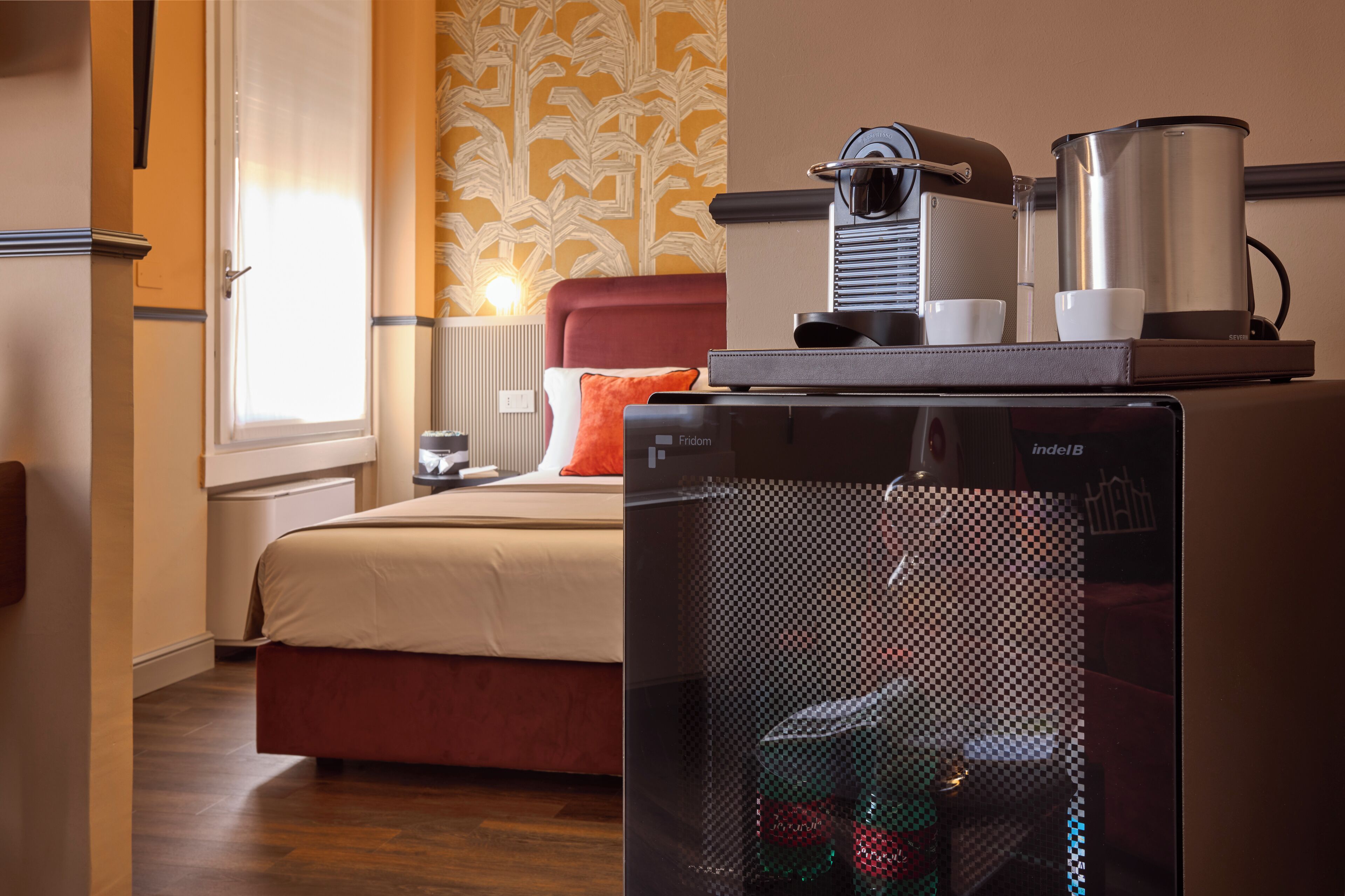 A hotel room with a bed, a coffee machine, and a refrigerator.
