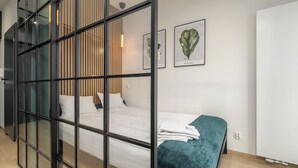 A modern hotel room with a large bed, a teal throw blanket, and a wooden slat partition.