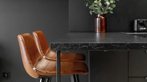 A modern kitchen with a dark countertop, a brown leather chair, and a potted plant.
