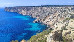 A coastal cliff with clear blue waters and rocky terrain.