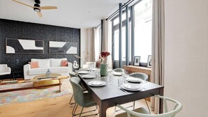 Un salon moderne avec un mur en briques noires, un canapé blanc et un coin repas avec une table en bois dressée pour quatre personnes.