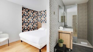 Une chambre d'hôtel moderne avec un papier peint à motifs, un lit blanc, une tête de lit en bois et une petite plante en pot.