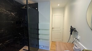 Een moderne badkamer met een glazen douchecabine, een witte wastafel en een houten opbergmeubel.