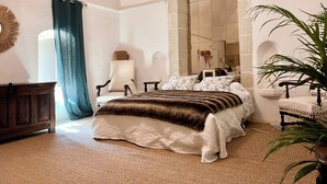 Ein Schlafzimmer mit einem großen Bett, einem Sessel, einem Spiegel und einer Pflanze.