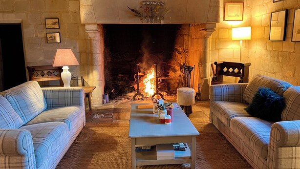 Ein gemütliches Wohnzimmer mit Kamin aus Stein, zwei Sofas, einem Couchtisch und gerahmten Bildern an den Wänden.
