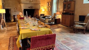 Une salle à manger avec une longue table dressée pour le repas, une cheminée et un coin salon confortable avec un canapé et des fauteuils.