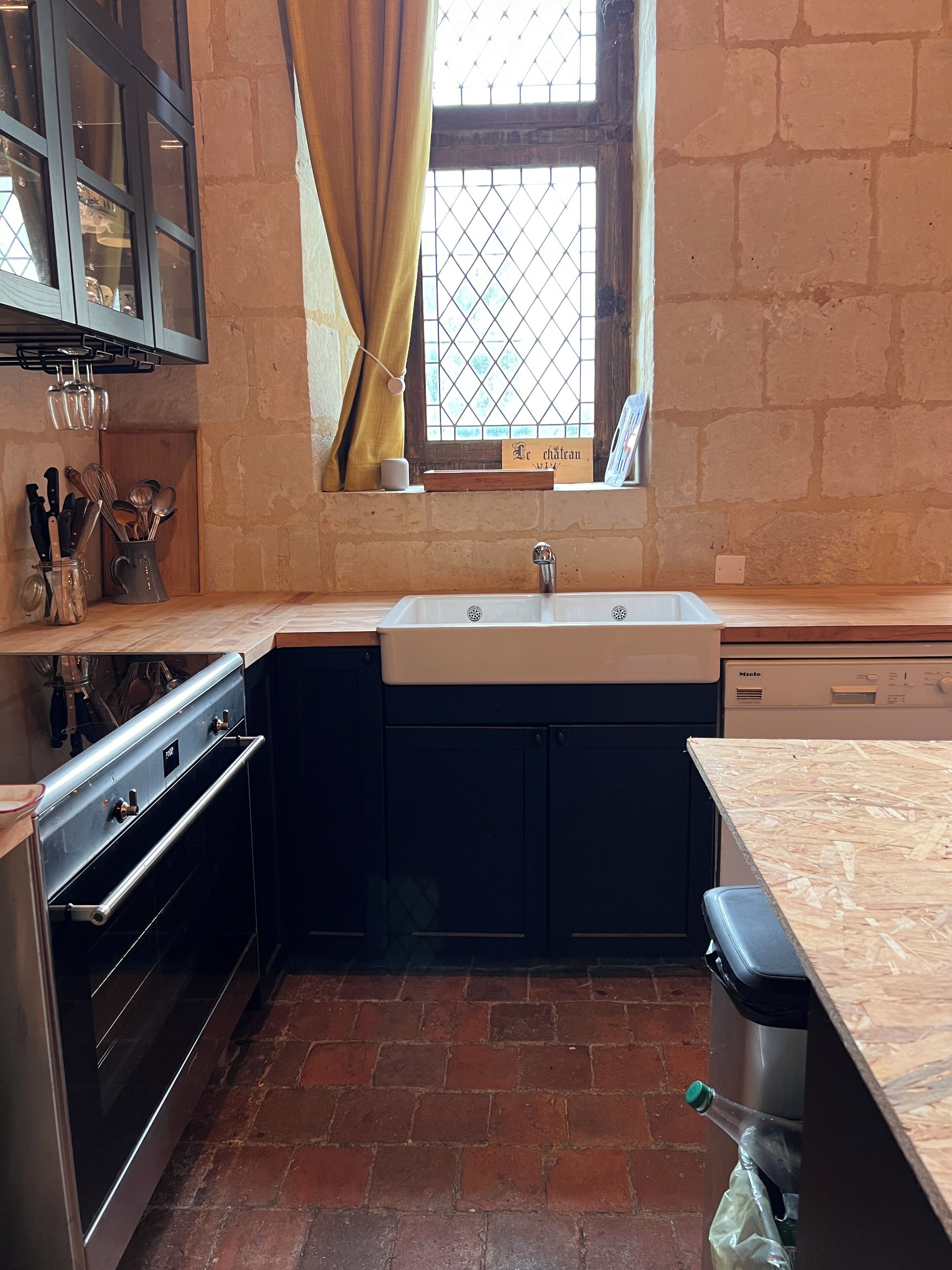 Una cucina con forno a incasso, lavello e finestra con tende.