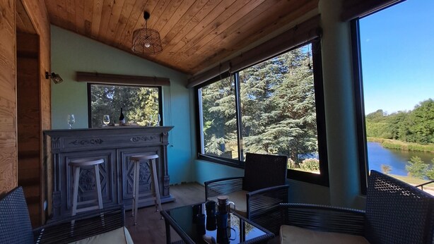 A wooden ceiling, a bar area with stools, wicker furniture, and large windows overlooking a natural landscape. - House overlooking private lake in mid-mountain setting. Peace and quiet in the heart of nature! (Pradelles-Cabardès)