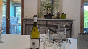 A dining table set with a bottle of wine, glasses, and plates, with a view of a balcony and a mirror above. - House overlooking private lake in mid-mountain setting. Peace and quiet in the heart of nature! (Pradelles-Cabardès)