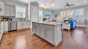 Una cocina amplia con una isla central, muebles blancos y un sofá azul en la sala de estar.