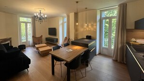 A modern living room with a wooden dining table, black sofas, and a chandelier. - Residence VillaBelleFleur-Apartment La Colchique (Château-Ville-Vieille)