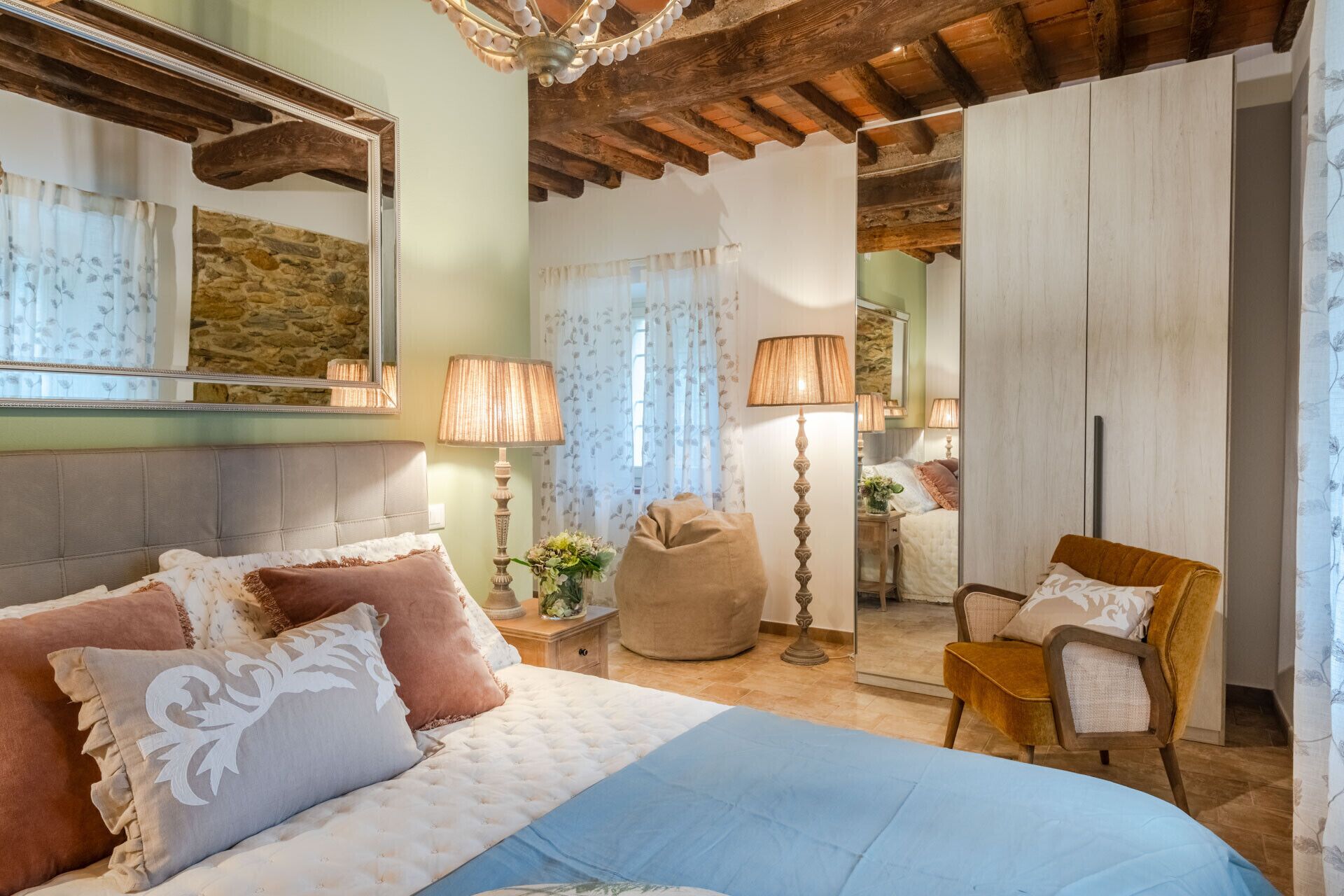 A bedroom with a bed, bedside lamps, a chair, and a mirror.