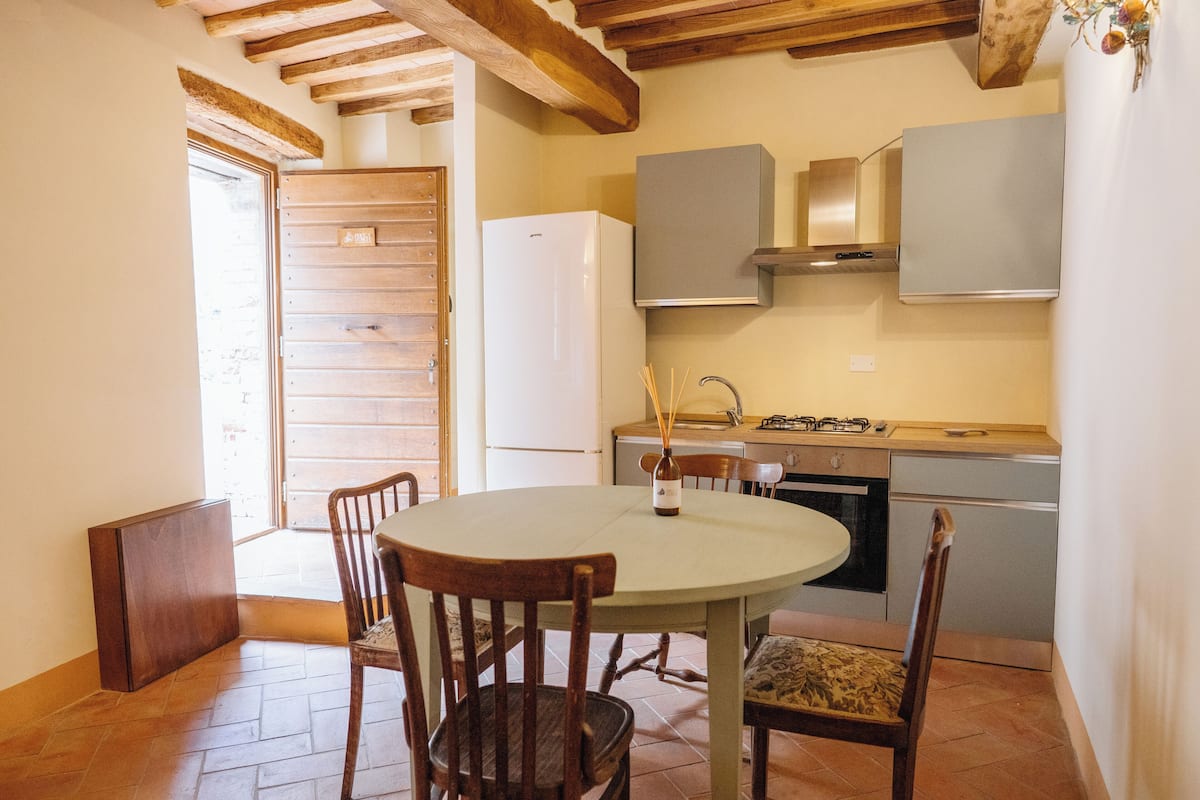 Een keuken met een ronde tafel, houten stoelen, een witte koelkast en een fornuis.