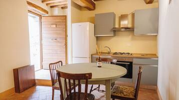 Una cocina con una mesa redonda, sillas de madera, un refrigerador blanco y una estufa.