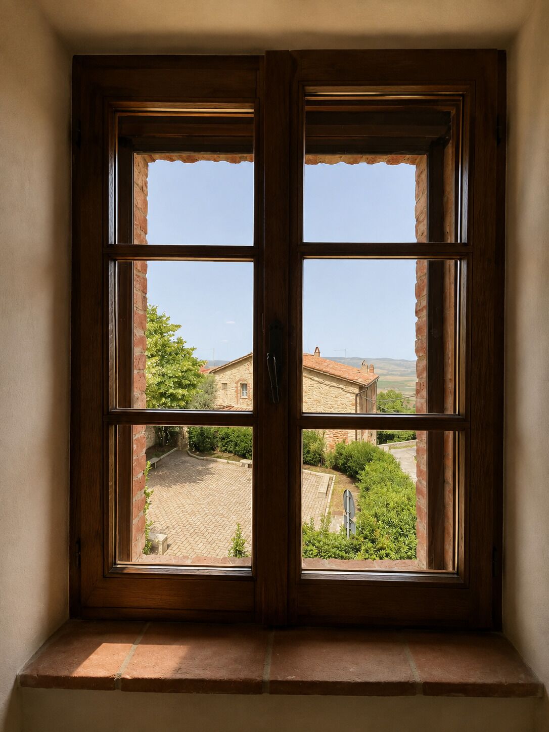 Una ventana con marco de madera que ofrece vista a un patio y un edificio de piedra.