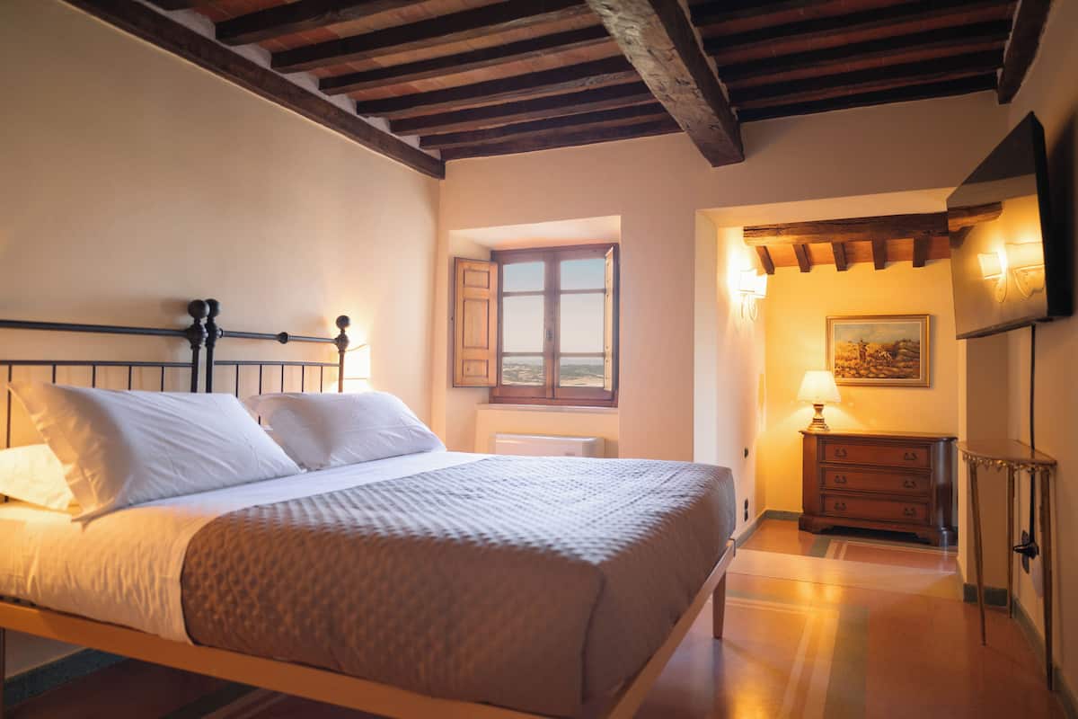 Een slaapkamer met een houten bed, een nachtkastje met een lamp, een dressoir en een schilderij aan de muur.