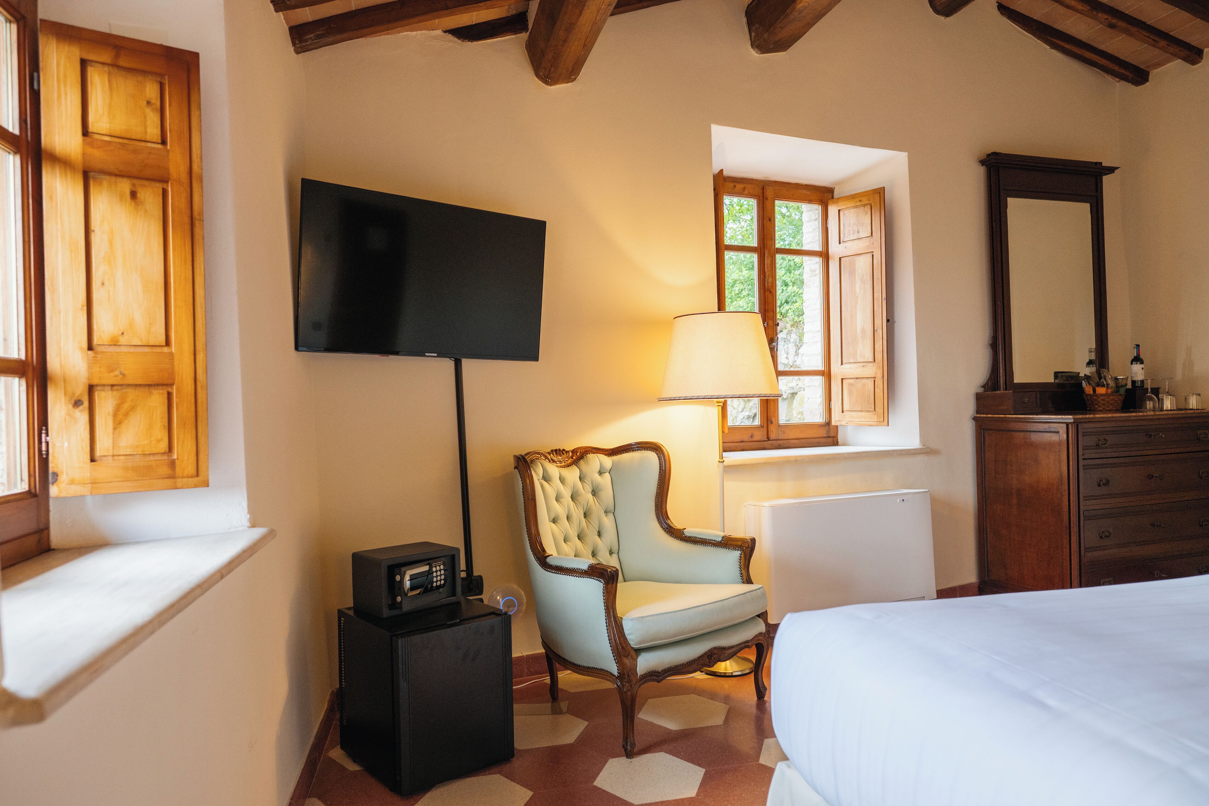 A bedroom with a bed, a television mounted on the wall, a wooden dresser, and a chair.
