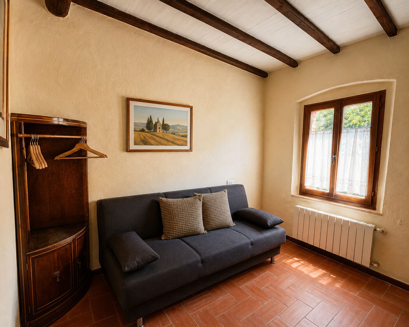 Ein Zimmer mit einem dunklen Sofa, einem Holzschrank, einem Gemälde und einem Fenster mit Blick.