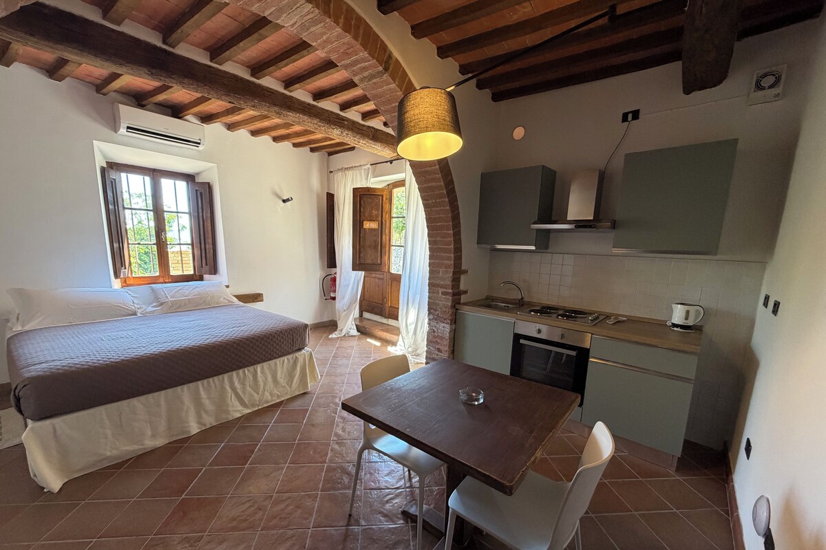 Un dormitorio con cama, una mesa de comedor con una silla, una cocina con estufa y una ventana.
