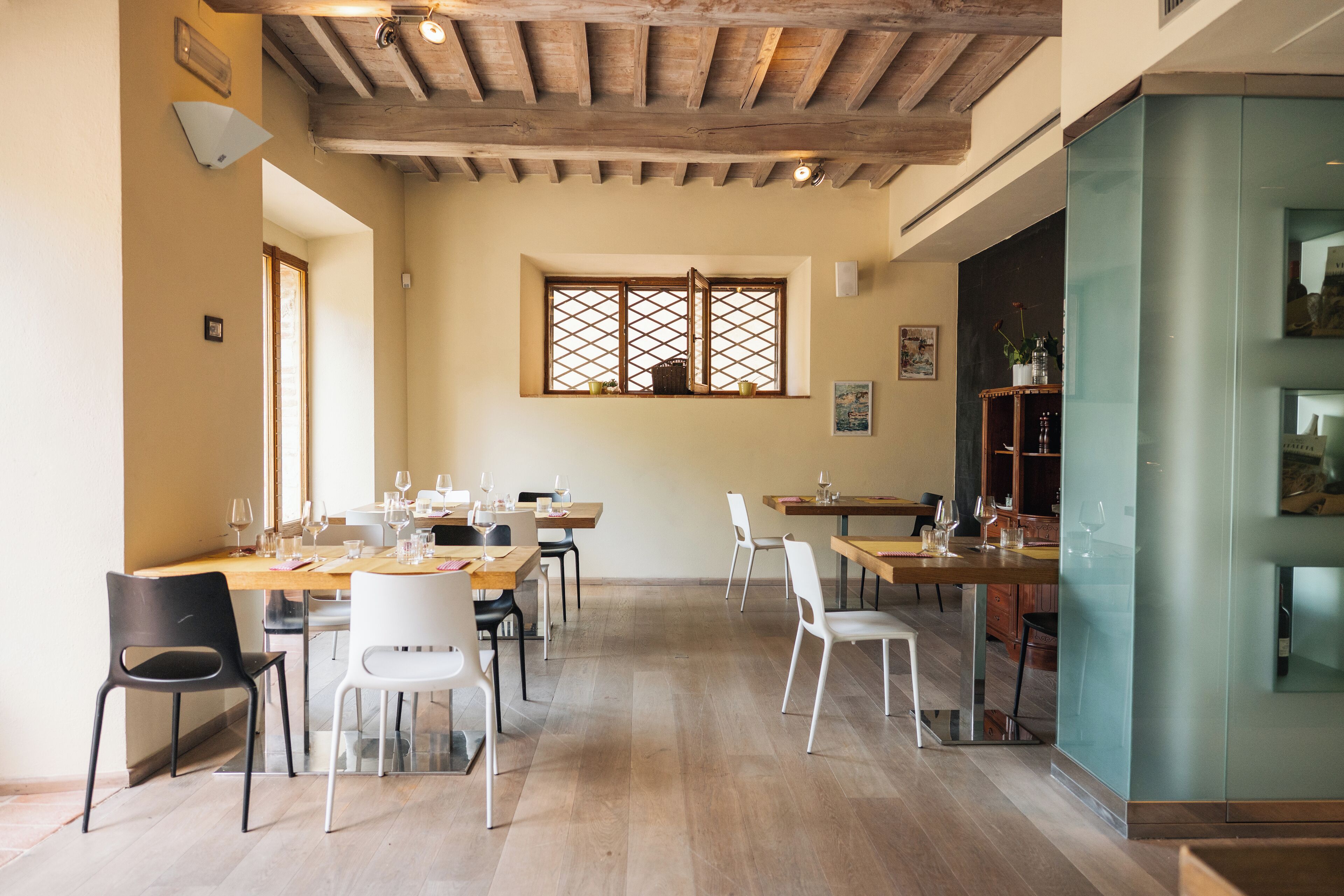 Un comedor con mesas y sillas de madera, un ventanal con diseño de celosía y una cocina moderna con separador de vidrio.