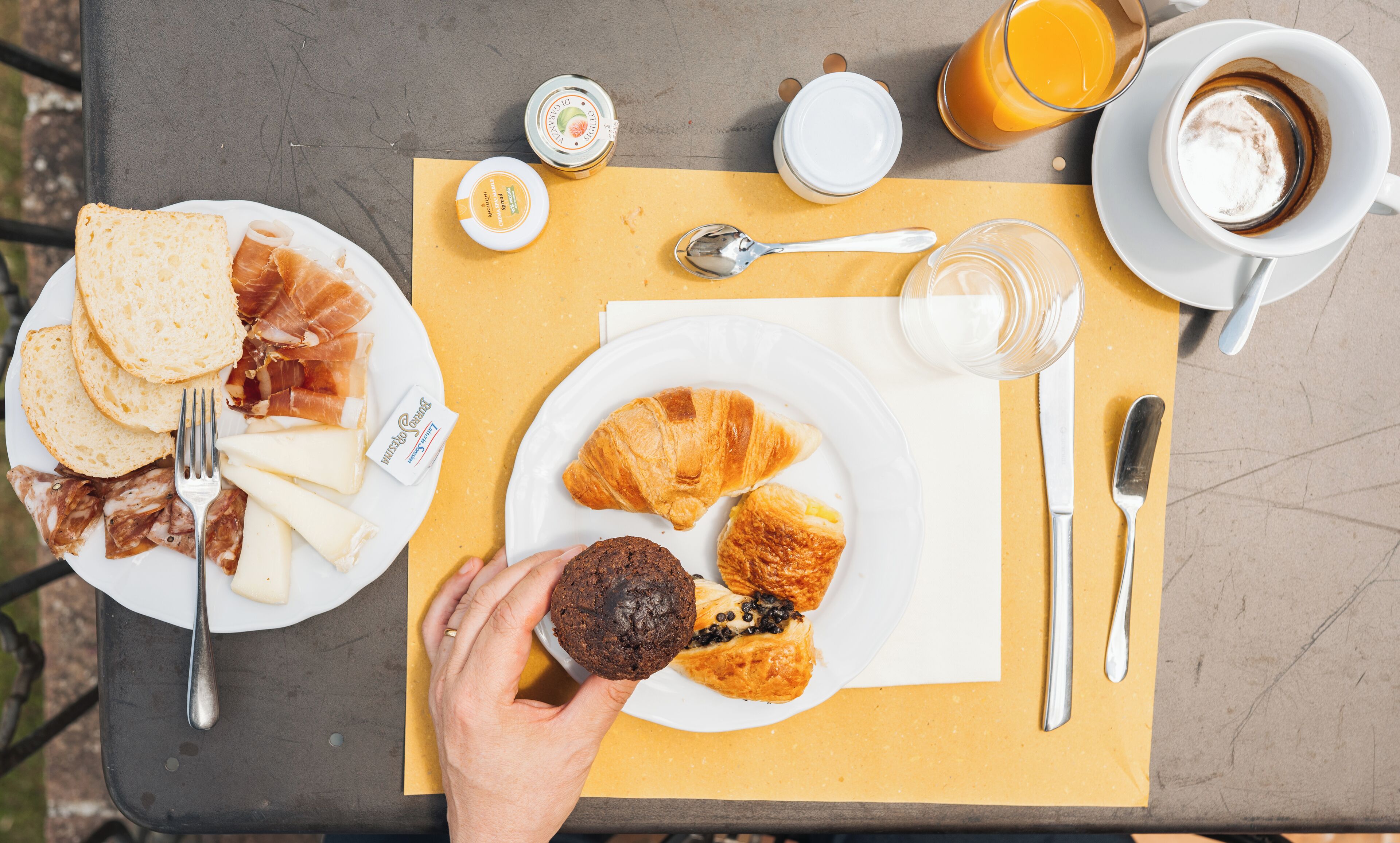 Une table de petit-déjeuner avec des croissants, un muffin et une assiette de fromage et de jambon.