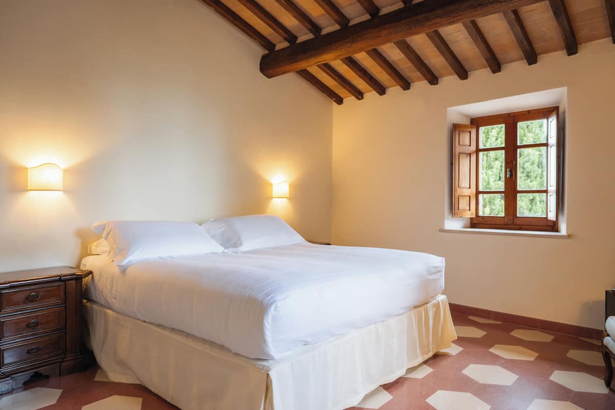 Een slaapkamer met een bed, nachtkastjes, een raam met uitzicht en een houten plafond.