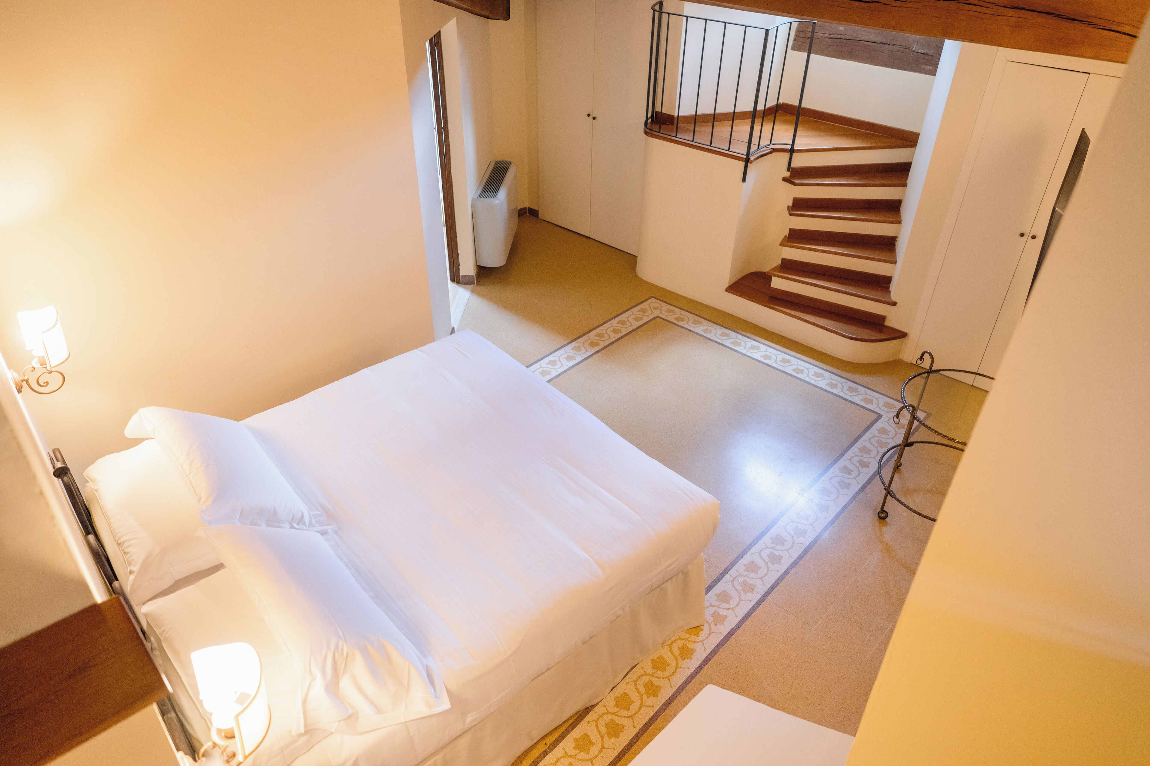 Un dormitorio con una cama, un radiador, una escalera y una alfombra estampada.