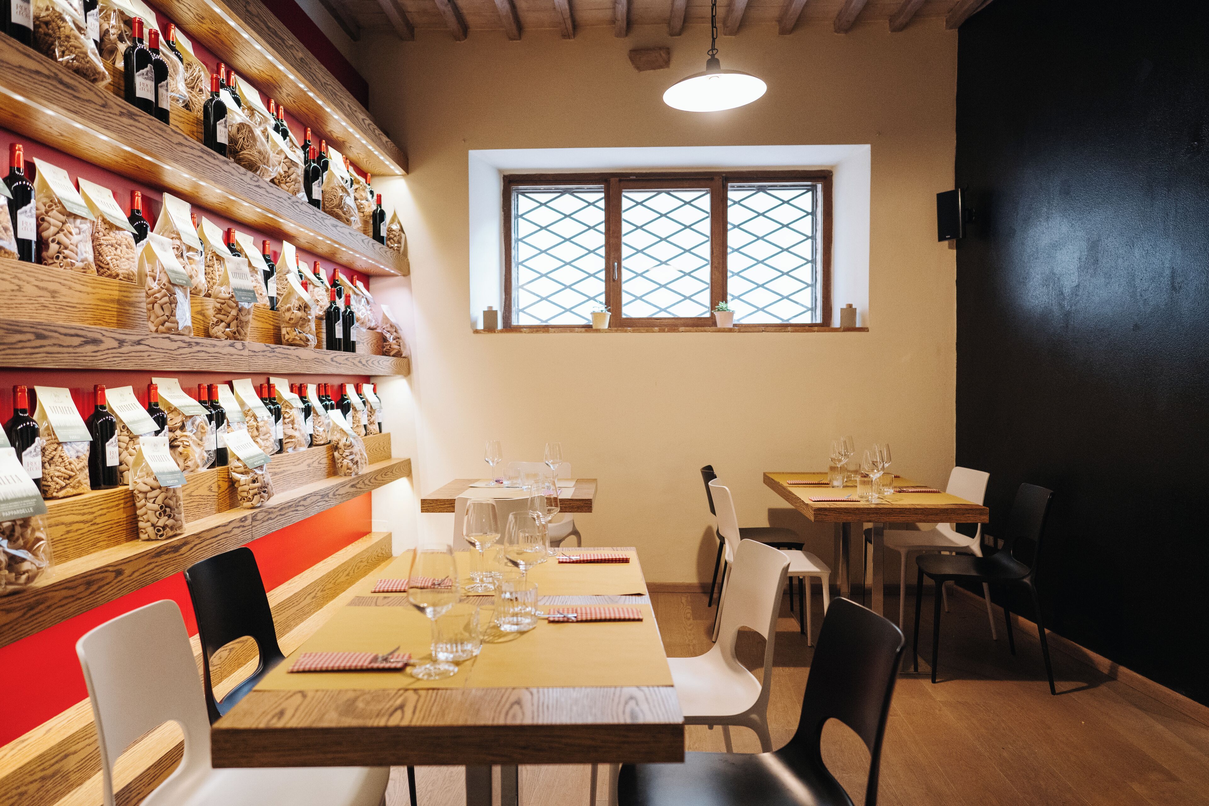 A restaurant interior with wooden shelves displaying bottles, a window with a lattice design, and tables set for dining.