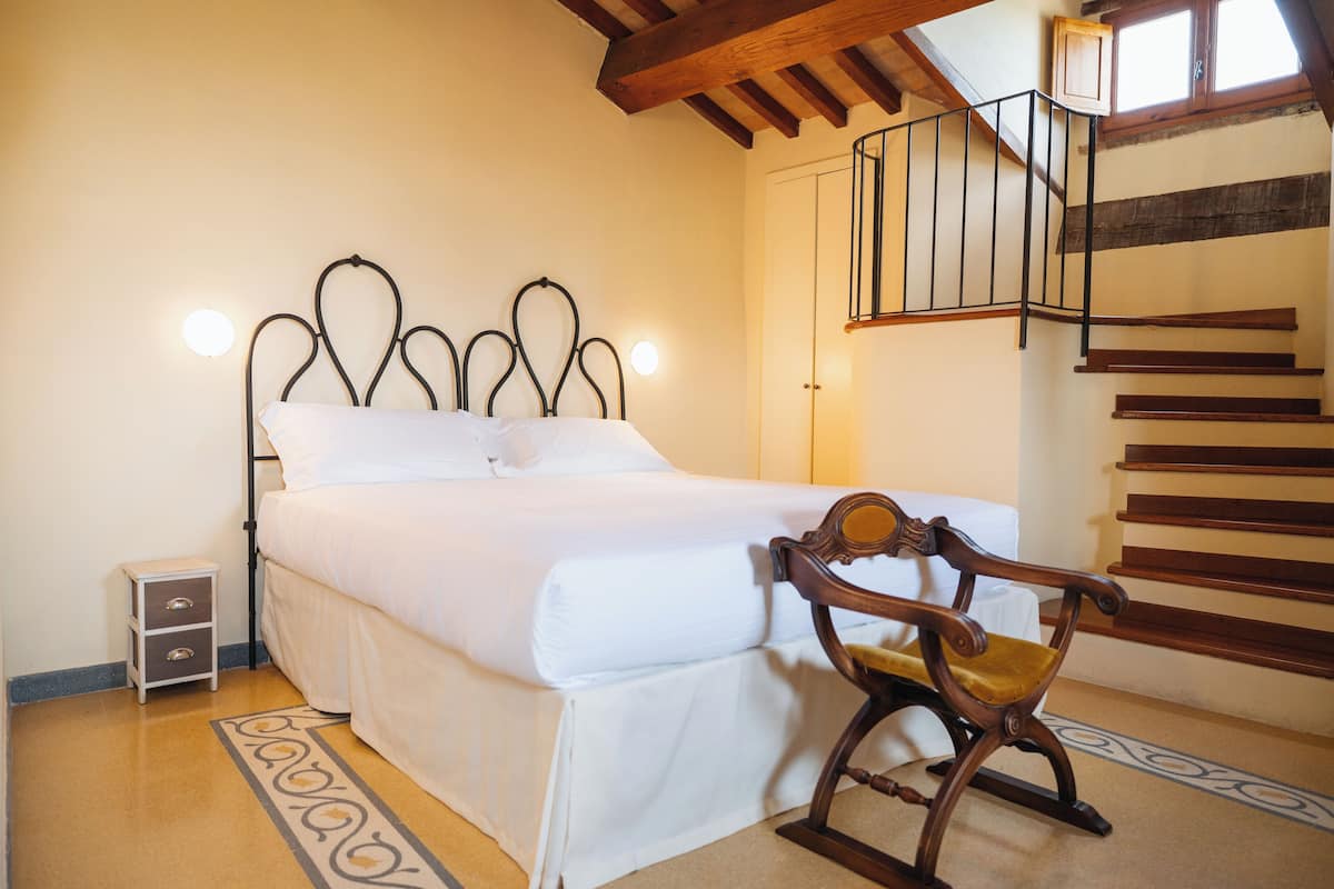 Een slaapkamer met een bed, nachtkastje, schommelstoel en een houten trap.