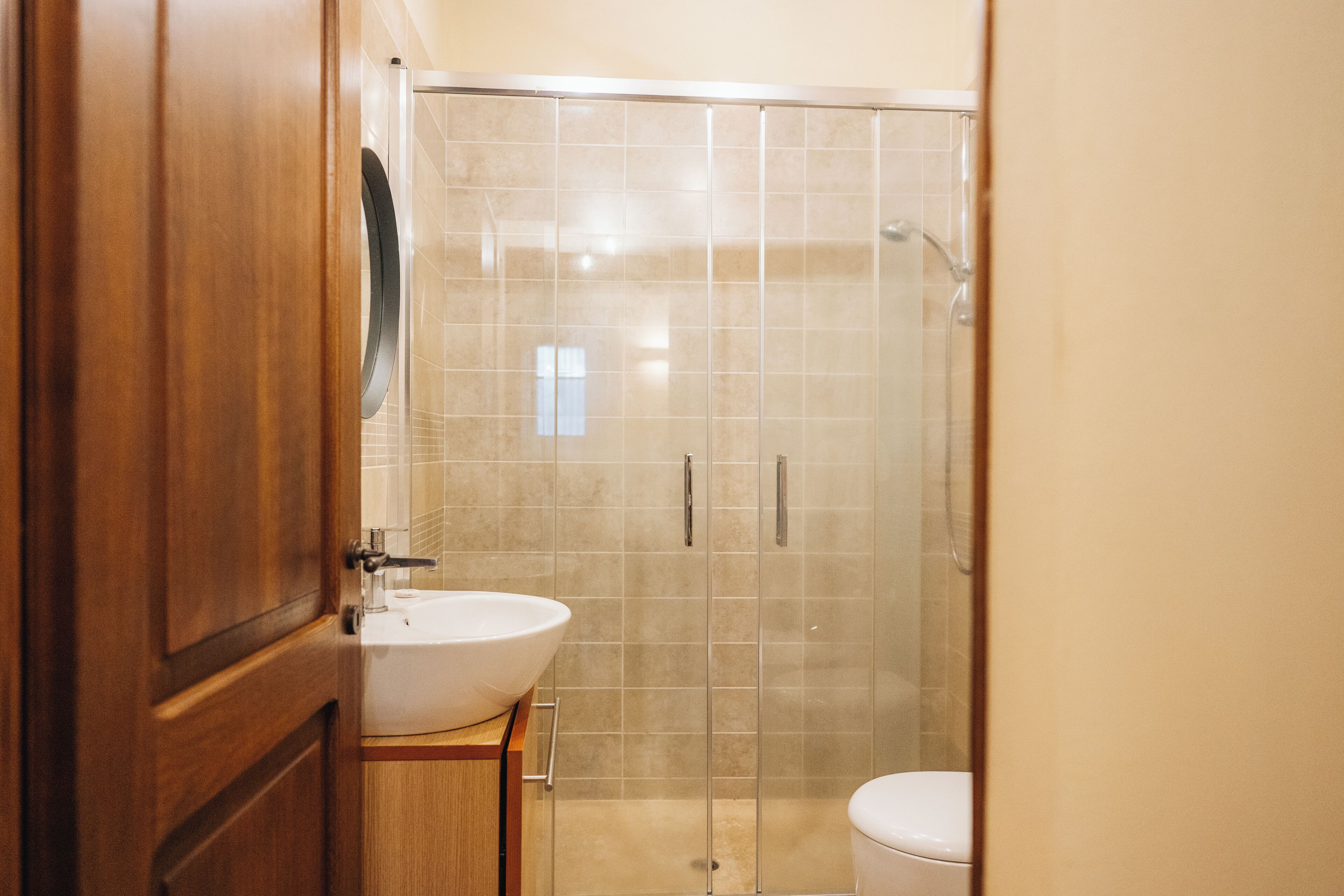 A bathroom with a wooden vanity, a white sink, and a glass-enclosed shower area.