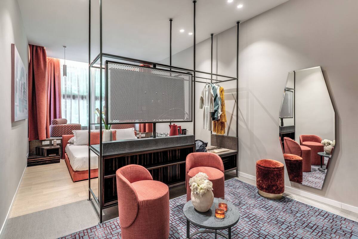 A modern hotel room with a bed, seating area, and a large mirror.