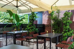 Terrassa exterior amb taules i caires, envoltada de vegetació i una tanca de fusta.