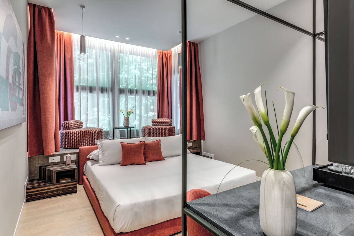 A modern hotel room with a large bed, a desk, and a vase of flowers.