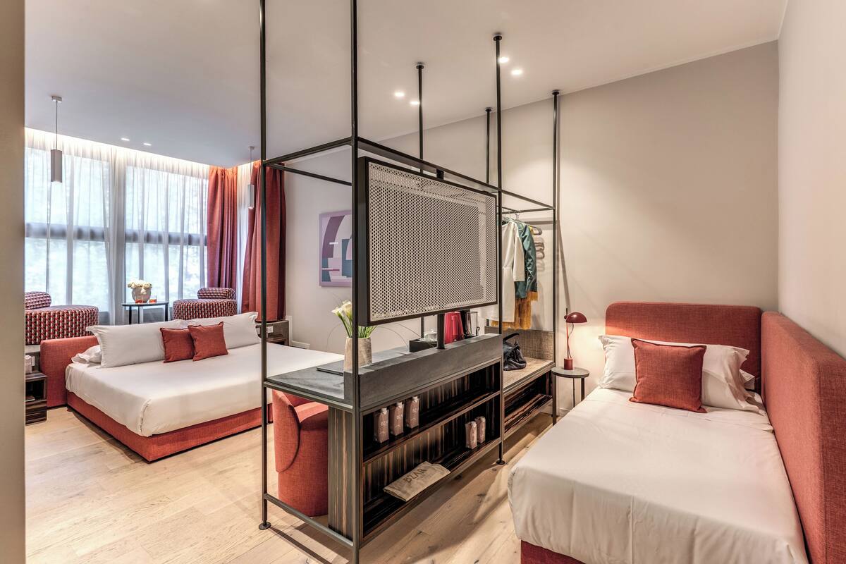 A modern hotel room with a glass partition, two beds, a desk, and a view of the water.
