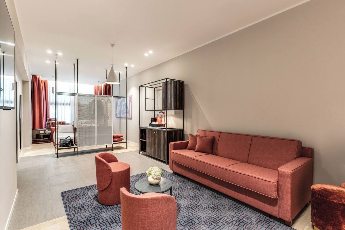 A modern living room with a red sofa, two armchairs, a coffee table, and a patterned rug.