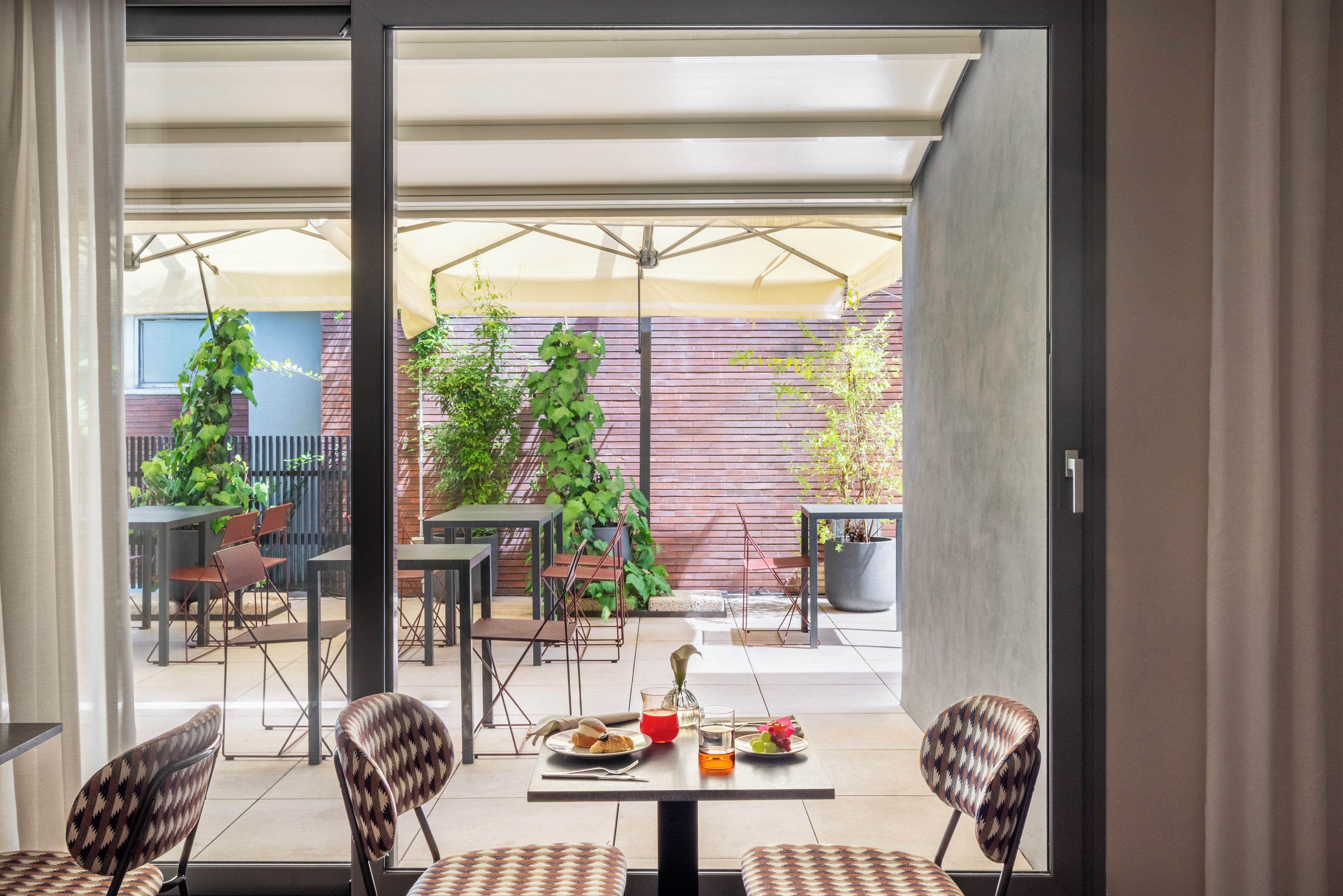 An outdoor patio with tables and chairs, a brick wall, and potted plants.