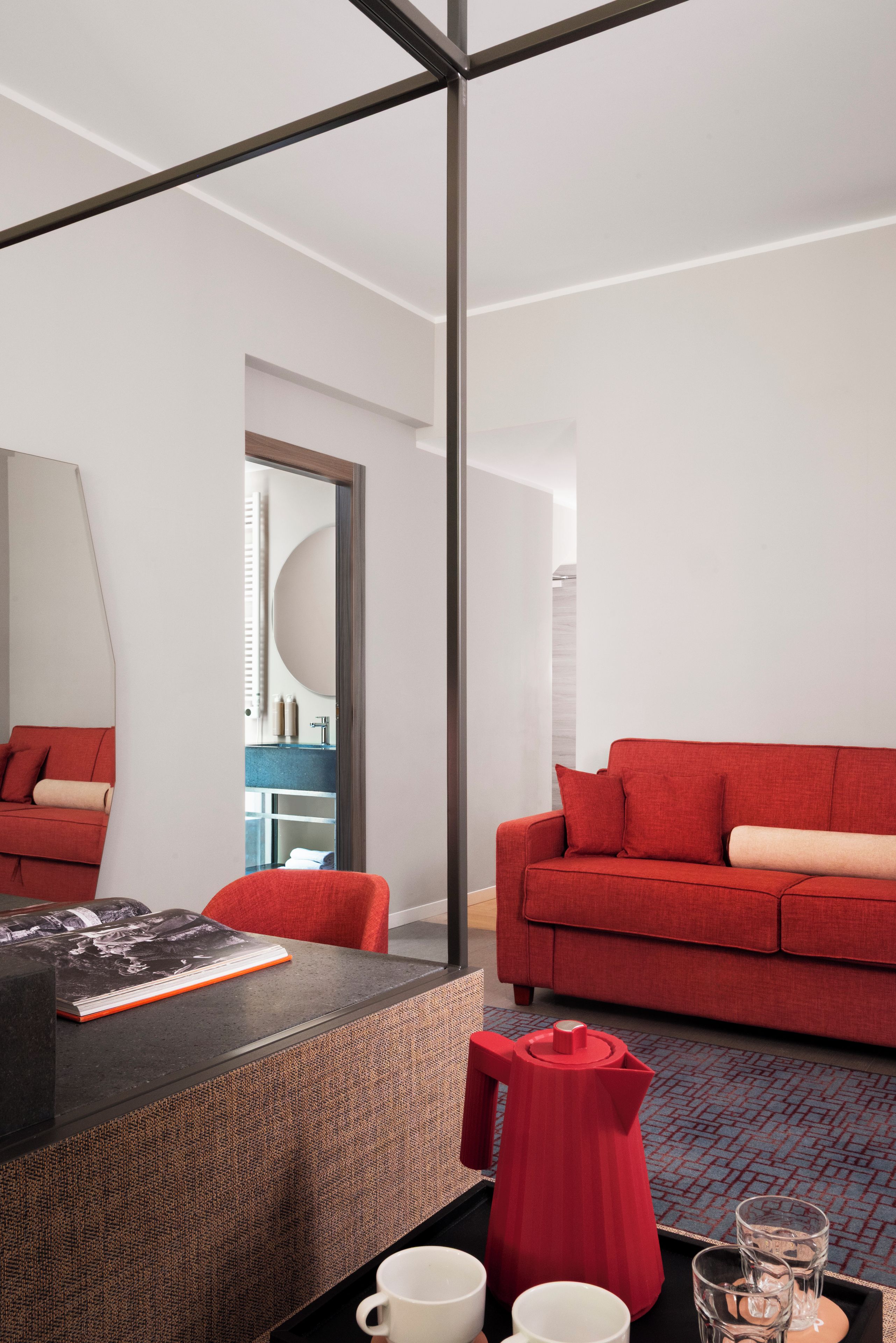 Une chambre d’hôtel moderne avec un grand lit, un canapé rouge, une table basse et un bureau avec un ordinateur portable.