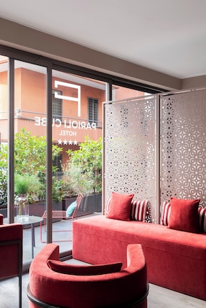 A modern hotel room with a red sofa, a glass partition, and a view of the outside. - PARIOLI CUBE HOTEL (Rome)