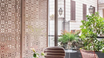 Un área de estar moderna al aire libre con una mesa de vidrio, sillas estampadas y un separador decorativo.