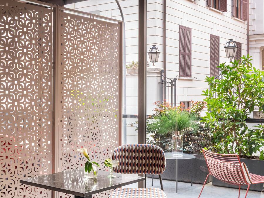 Un área de estar moderna al aire libre con una mesa de vidrio, sillas estampadas y un separador decorativo.