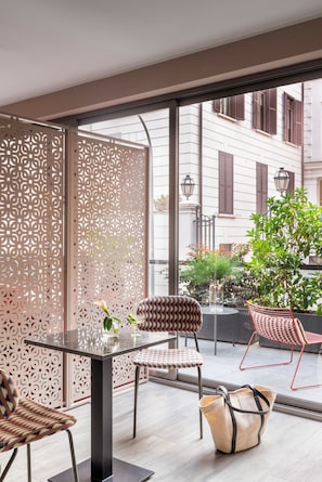 A modern outdoor seating area with a glass table, patterned chairs, and a decorative partition.