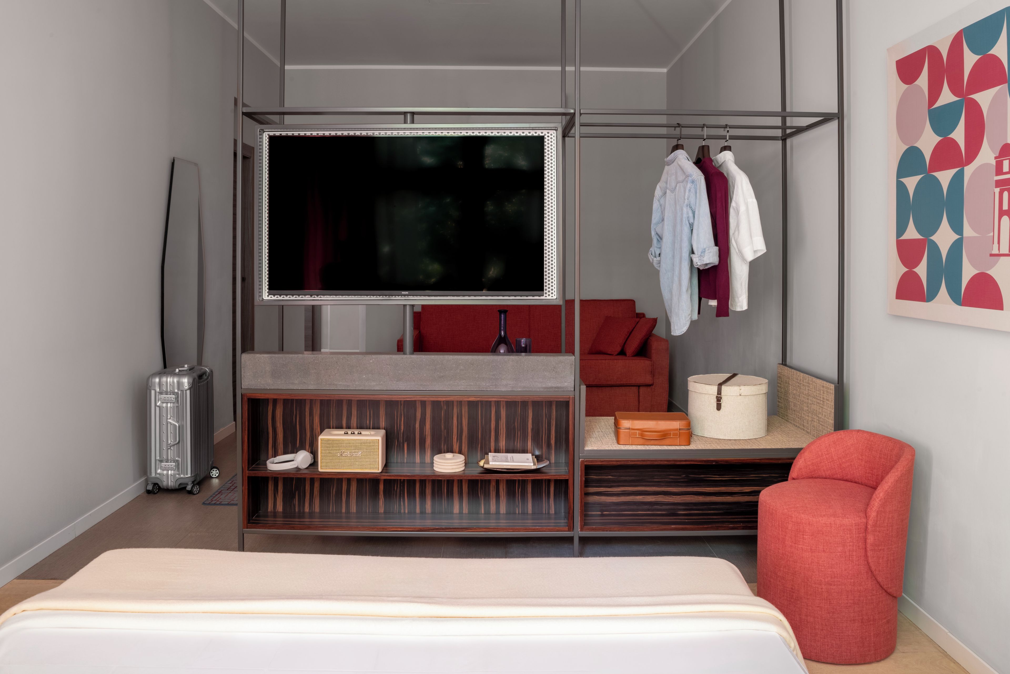 A modern bedroom with a bed, a TV, a wardrobe, a red sofa, and a red chair.