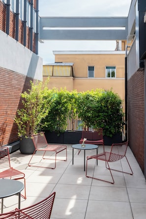 An outdoor patio with red metal chairs and tables, surrounded by a low brick wall and a hedge. - PARIOLI CUBE HOTEL (Rome)