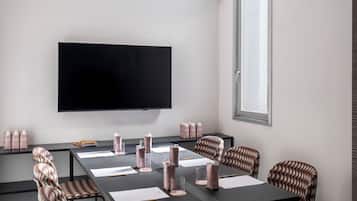A modern meeting room with a large flat-screen TV, a long table with chairs, and a window providing natural light.