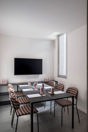 Una sala de reuniones moderna con una televisión de pantalla plana grande, una mesa larga con sillas y un ventanal que proporciona luz natural.