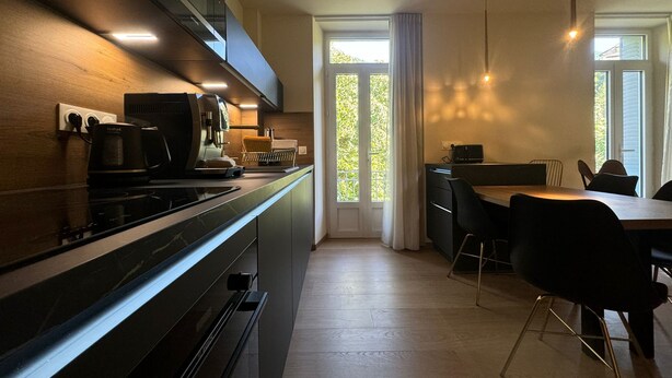 A modern kitchen with a built-in stove, a coffee machine, and a dining area with a table and chairs. - Residence VillaBelleFleur-Apartment La Centaurée (Château-Ville-Vieille)