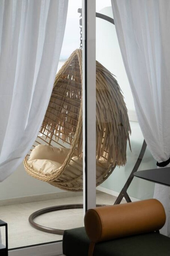 Una habitación con una silla colgante, cortinas blancas y vistas a través de un ventanal.